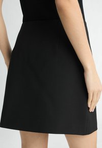 Schwarzer Minirock aus glattem Stoff, mit einer figurschmeichelnden Silhouette und seitlichen Eingrifftaschen, in einem klaren, minimalistischen Design.