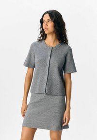 Grå ribstrikket kortærmet cardigan med knapper og rund halsudskæring, parret med en matchende ribstrikket nederdel i en lignende nuance.