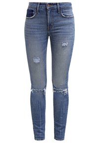 Jeans ajustados de denim, con un lavado azul medio, agujeros desgastados en las rodillas, dobladillo deshilachado y un sutil desvanecimiento en los muslos.