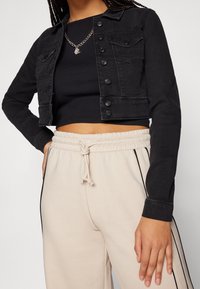 Černá džínsová zkrácená bunda s knofl�íkovým zapínáním a dvěma náprsními kapsami, nošená přes černý ribovaného topu a béžové jogger kalhoty s bočními pruhy.