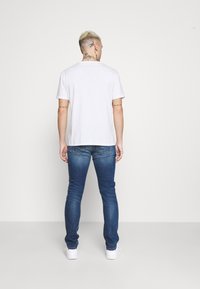 Vit kortärmad t-shirt i kombination med blå slim-fit jeans, med en standard passform och en ren design. Snygga vita sneakers fulländar looken.