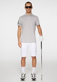 Light gray polo shirt with short sleeves, featuring a patterned cuff. Paired with white shorts and black and white golf shoes, holding a golf club.