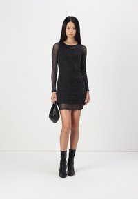 Μαύρο, εφαρμοστό φόρεμα μακρύ μανίκι από διάφανο, λαμπερό ύφασμα, με ελαφρώς διαφανή τελείωμα. Συνδυασμένο με μαύρες μπότες μέχρι τον αστράγαλο και μια μικρή τσάντα.