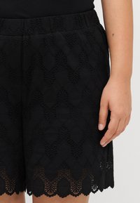 Pantaloni corti neri in pizzo con orlo scallopato, caratterizzati da un design a motivo. La vita è elastica, aumentando il comfort e la vestibilità.