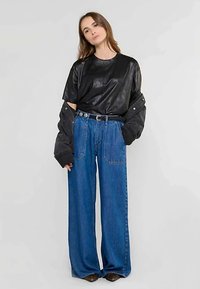 T-shirt oversize en cuir noir, jean bleu taille haute à jambes larges avec ceinture, et manches noires. Texture lisse et poches proéminentes.