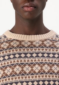 Strikket sweater med et mønster i creme, brun og marineblå geometriske former, med en klassisk rund hals og ribbet halsudskæring. Struktureret stof.