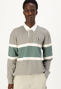 Langærmet poloshirt i grå med grønne og hvide vandrette striber. Har en krave og et skjoldlogo på brystet. Blødt bomuldsstof.