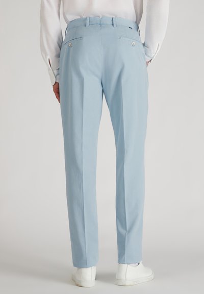 Jasnoniebieskie spodnie wykonane z gładkiego materiału, o prostym kroju, z dwiema tylnymi kieszeniami zapinanymi na guziki, noszone z białymi sneakersami.