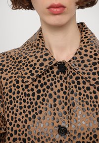 Animal print coat in tan with black and metallic spots. Features a classic collar and front button closure. Smooth texture, lightweight fabric.