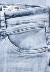 Tasca di jeans in denim azzurro chiaro con passante per cintura visibile, dettagli di cucitura, rivetto metallico e etichetta con la scritta "LOOSE" e "DENIM STREET ONE."