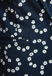 Marinblått tyg med ett blommönster bestående av små vita och ljusblå blommor, med en enda knapp och en bröstficka.