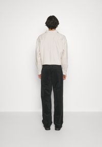 Long-sleeve, light beige shirt made of soft fabric, paired with black, loose-fitting trousers with a smooth texture.