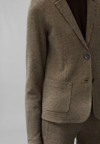 Hnědý houndstooth blejzr s klopou, jedním knoflíkem a nášivkovou kapsou. Vyrobeno z texturované látky, zdobené černými knoflíky.