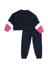 Navyblå träningsoverall med en kort sweatshirt och matchande byxor. Har rosa, vita och gula detaljer på ärmar och manschetter. Mjuk tyg.