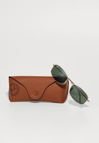 Ray-Ban žalių lęšių saulės akiniai su auksiniu rėmeliu, gulintys ant rudos tekstūruotos odinės dėžutės su Ray-Ban logotipu ir UV apsaugos etikete.