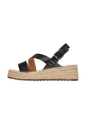 Czarne skórzane sandały na klinie z grubą plecioną podeszwą z juty, z paskiem krzyżującym się na stopie, regulowanym paskiem na kostkę oraz teksturowaną podeszwą zapewniającą przyczepność.