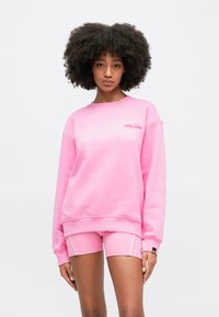 Ružová mikina s okrúhlym výstrihom a rebrovanými rukávmi, s malým logom na hrudi. Skombinovaná s ružovými šortkami s bielymi akcentmi.