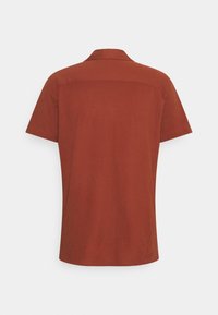 Kratší rukáv, košilové tričko v měděné oranžové barvě, vyrobené z měkké tkaniny. Má hladkou texturu a čisté linie bez viditelných vzorů nebo akcentů.