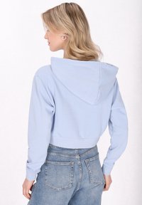 Hoodie corto azzurro con cappuccio regolabile, polsini a costine e una texture liscia, abbinato a jeans blu scoloriti a vita alta.