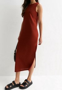Abito senza maniche di colore ruggine con texture ondulata e spacco laterale. Abbinato a sandali neri piatti con fasce larghe e suola platform.