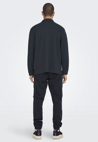 Musta pitkähihaisen paidan suoraleikkaus yhdistettynä tummiin cargo-housuihin, joissa on sivutaskut ja vartalonmyötäiset resorit. Rentoon lookiin sopivat arkikengät täydentävät asun.