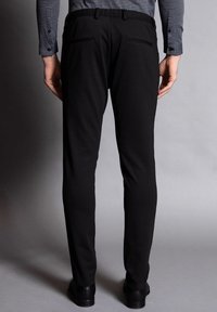 Svarta byxor med slim fit, elastisk midja, bakfickor och slät tygtextur, i kombination med en mönstrad skjorta.