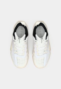 Weiße Sportschuhe mit Obermaterial aus Mesh, strukturierten Mustern, schwarzer Einfassung und beiger Gummisohle; verfügen über Schnürsenkel und Branding auf der Zunge.