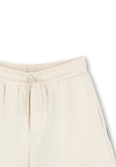 Pantalons de jogging beige clair avec une taille élastique et un cordon de serrage, des poches latérales et une texture lisse et douce.