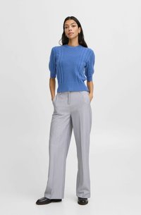 Helles blaues Strickpullover mit strukturierten Mustern, kombiniert mit grauen weit geschnittenen Hosen. Das Outfit zeichnet sich durch kurze Ärmel und eine taillierte Passform aus.