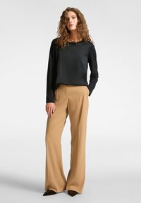 Schwarzes langärmliges Oberteil mit rundem Ausschnitt, kombiniert mit hellbraunen weiten Hosen. Glatter Stoff, minimalistisches Design, keine sichtbaren Muster.
