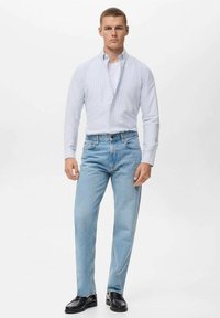 Vaqueros de mezclilla azul claro con corte recto, combinados con una camisa de botón ajustada, de rayas azul claro y zapatos negros.