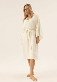 Kremowy szlafrok z szerokimi rękawami, wiązaniem w pasie i bocznymi rozcięciami. Gładka tekstura, długość do kolan i prosty design.