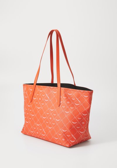Orange Tragetasche aus strukturiertem Material, mit einem sich wiederholenden weißen Muster, zwei langen Griffen und einem schwarzen Innenraum.