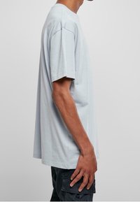 Světle modré oversized tričko z bavlny, s krátkými rukávy, kulatým v�ýstřihem a volným střihem. Textura vypadá jemně a hladce.