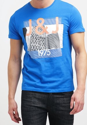 Blå bomuldst-shirt med korte ærmer, der har et grafisk print af "J&J 1975" og abstrakte designelementer. Tekstureret stof med en klassisk pasform.