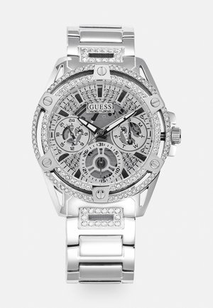 Montre en acier inoxydable argenté pour homme avec accents en cristal, cadran transparent, plusieurs sous-cadrans et un design de boîtier audacieux et géométrique.