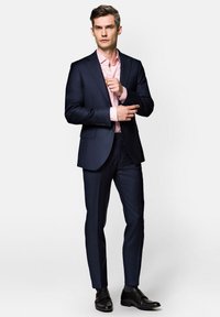 Granatowa marynarka na różowo paskowaną koszulę, dopasowany krój. Ciemne spodnie i czarne buty. Gładka tkanina, minimalistyczny design i eleganckie detale.