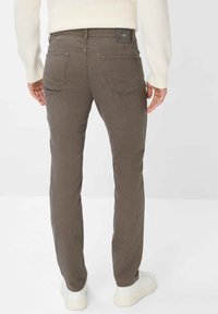 Jeans slim fit marroni con una trama texturizzata, dotati di due tasche posteriori e un'etichetta con il logo in vita. Abbinati a sneaker bianche.