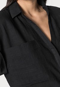 Svart linnenärmad skjorta med krage, korta ärmar och bröstficka. Har en texturerad yta och en avslappnad passform.