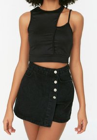 Černý zkrácený top na ramínka s jedním ramenním páskem a prošitými detaily, v kombinaci s černou džínovou sukní vysokého pasu s nerezovými knoflíky.