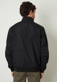 Sort nylon bomberjakke med ståendet krave, elastiske ærmer og talje. Glat overflade med minimal design detaljer på ryggen.
