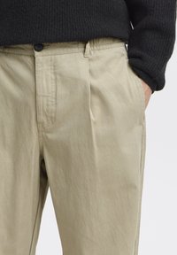 Beige Baumwollhosen mit geradem Schnitt, ausgestattet mit Knopfverschluss, Seitentaschen und einem elastischen Bund für mehr Komfort.