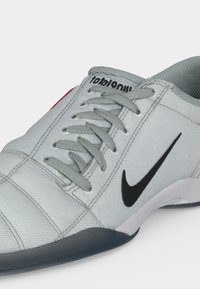 Baskets Nike grises et blanches avec logo swoosh noir, lacets gris et col rembourré, présentées en gros plan sur fond blanc.