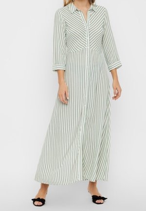 Striped, button-up maxi dress in light green and white. Features long sleeves and a flowing silhouette. Worn with black slip-on shoes.