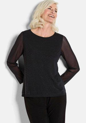 Schwarzes Langarmoberteil mit rundem Ausschnitt, das ein strukturiertes Design mit kleinen Verzierungen auf der Vorderseite und transparenten Ärmeln aufweist.