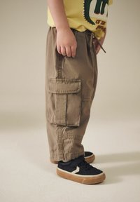 Khaki cargo bukser med lommer på siderne, parret med sorte sneakers med et hvidt og tan design.