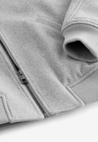 Gray zip-up jacket made of soft fabric, featuring ribbed cuffs and a visible front zipper. Smooth texture with a structured design.