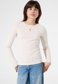 Lichtbeige geribde longsleeve top met een ronde hals, gecombineerd met blauwe high-waisted jeans. Inclusief een gouden hanger ketting.