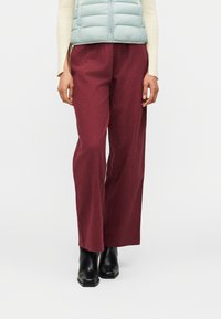 Άτομο που φοράει μπορντό φαρδιά παντελόνια, μαύρα μποτάκια αστραγάλου, εκρού ριμπ μακρυμάνικη μπλούζα και γαλάζιο καπιτονέ γιλέκο.