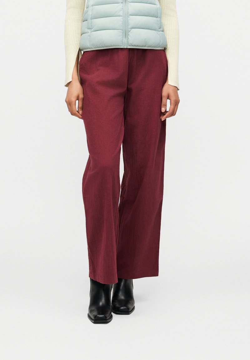 Άτομο που φοράει μπορντό φαρδιά παντελόνια, μαύρα μποτάκια αστραγάλου, εκρού ριμπ μακρυμάνικη μπλούζα και γαλάζιο καπιτονέ γιλέκο.